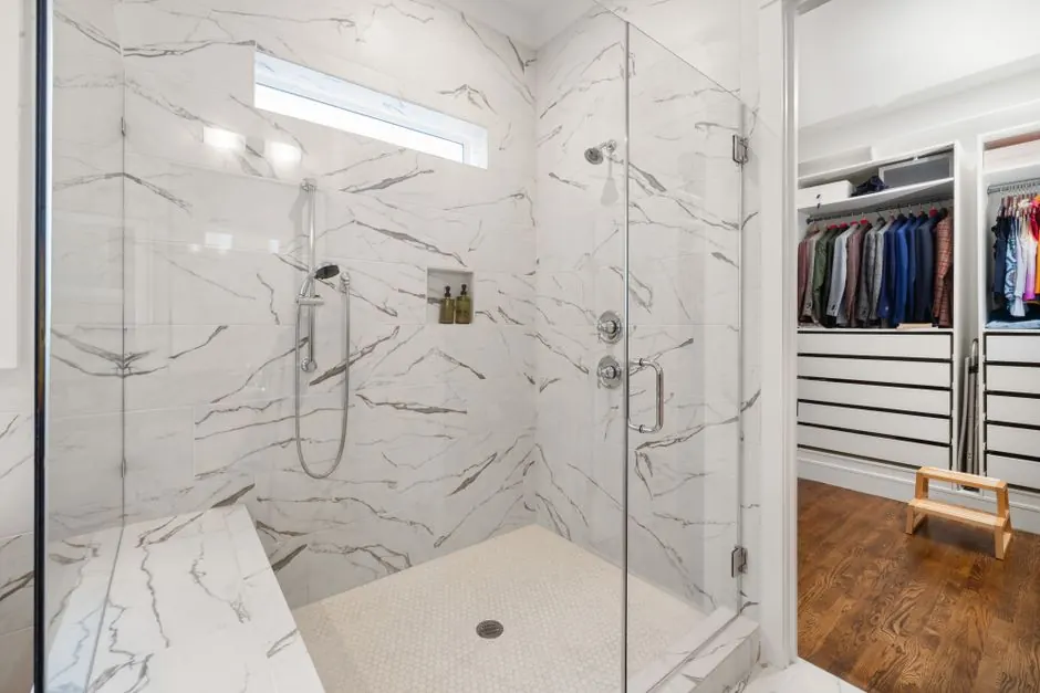 Luxurious marble shower design with glass doors, adjacent to an organized walk-in closet.