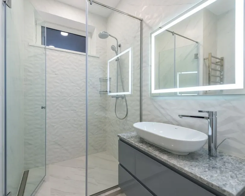 Stylish mirror illumination shining in bathroom above sink with faucet and shower cabin
